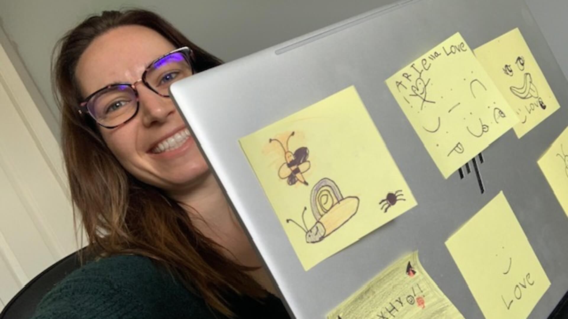 Brittany sitting with her laptop that has yellow sticky notes with messages from her daughters on the laptop lid
