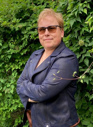 Carrie Anton in a blue jacket in front of green foliage