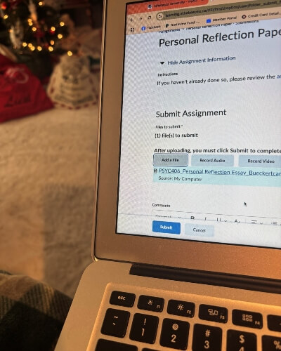 laptop screen displaying text from an assignment on a couch cushion with a Christmas tree in the background