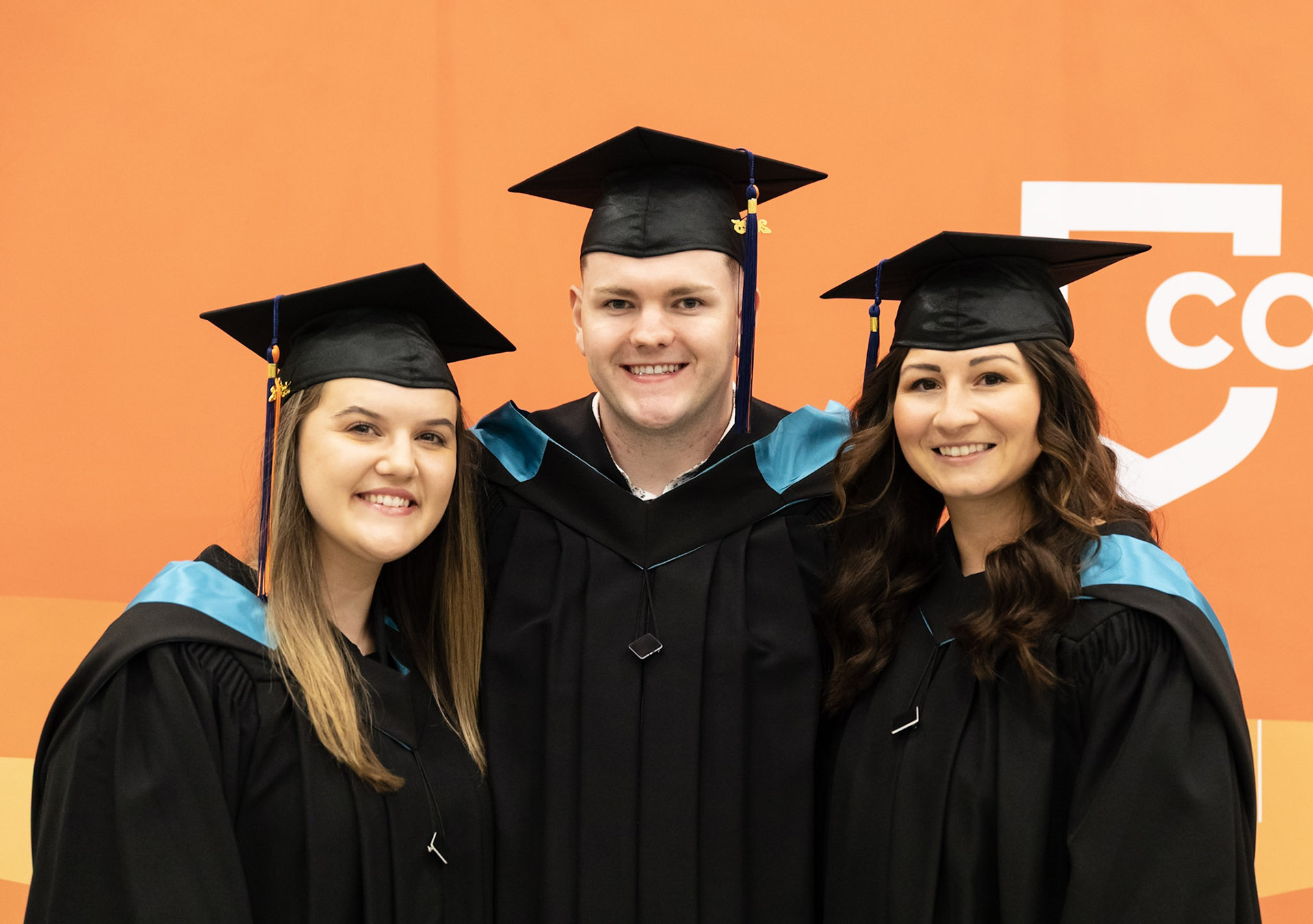 a trio of grads in front of an orange AU banner