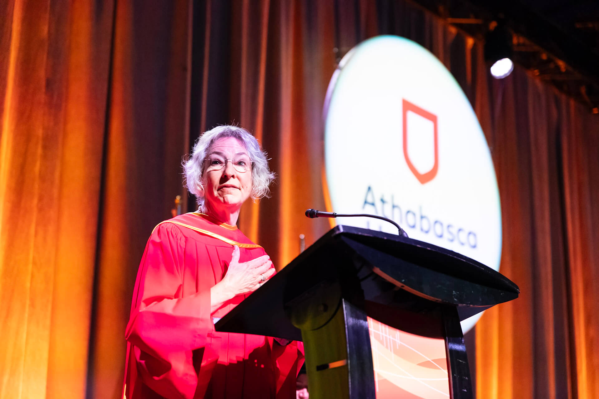 Joy Romero dressed in academic robes speaks at a podium