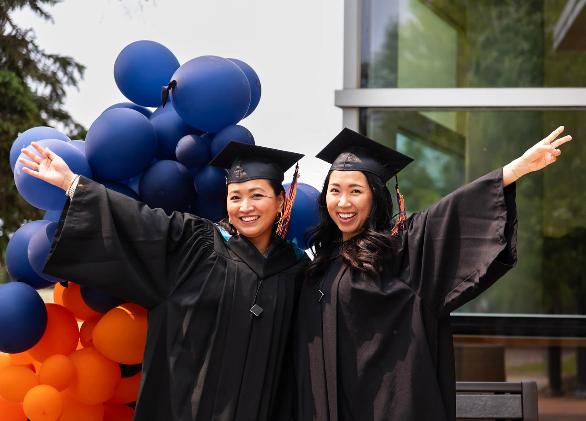 two grads pose for a photo on campus with balloons in the background