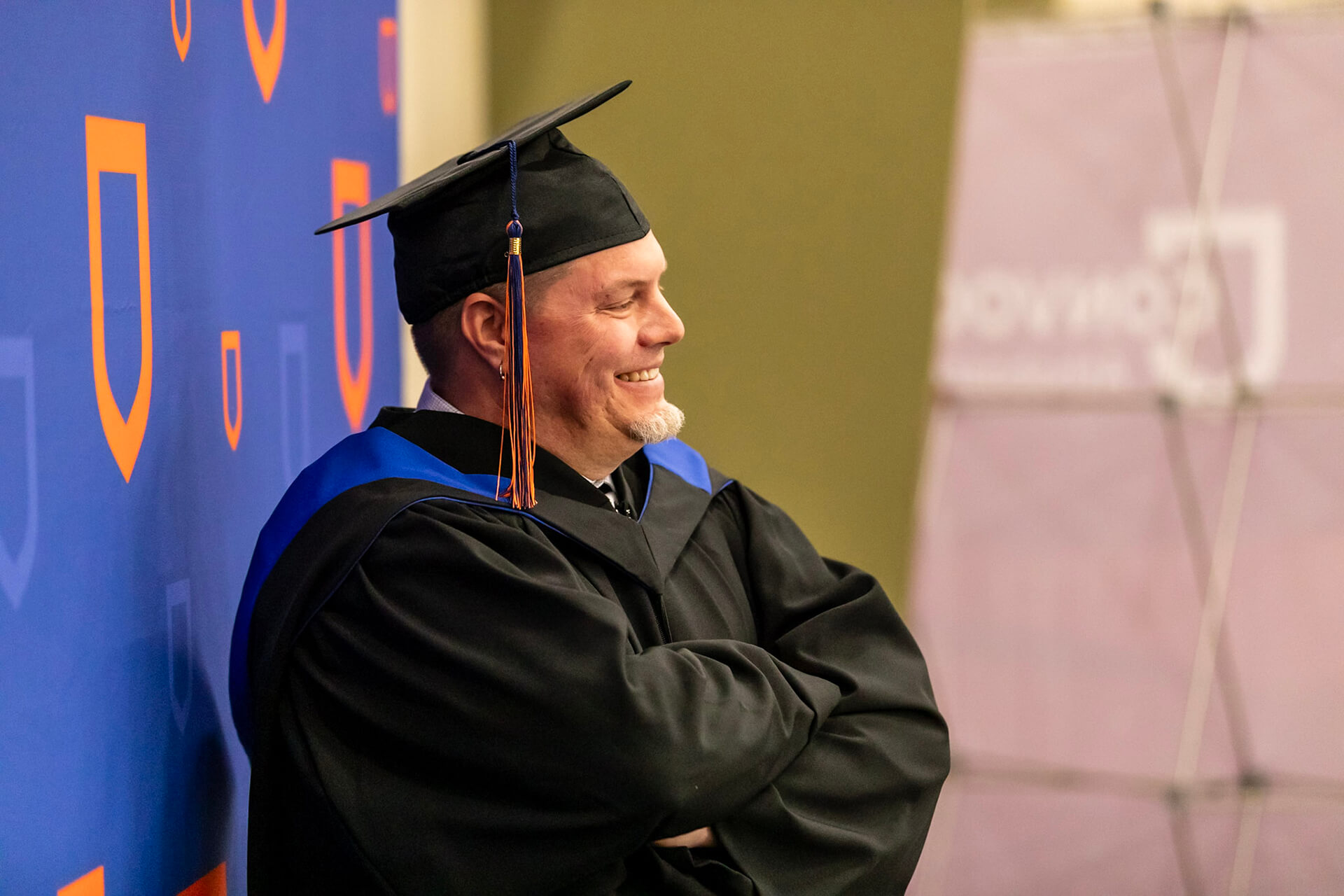 A proud grad poses for a photo in front of a banner