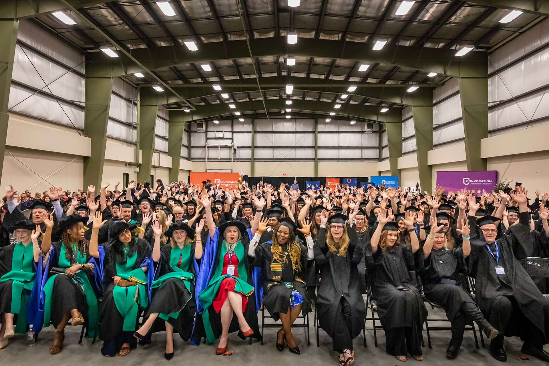 A room full of AU grads hold their hands in the air while seated