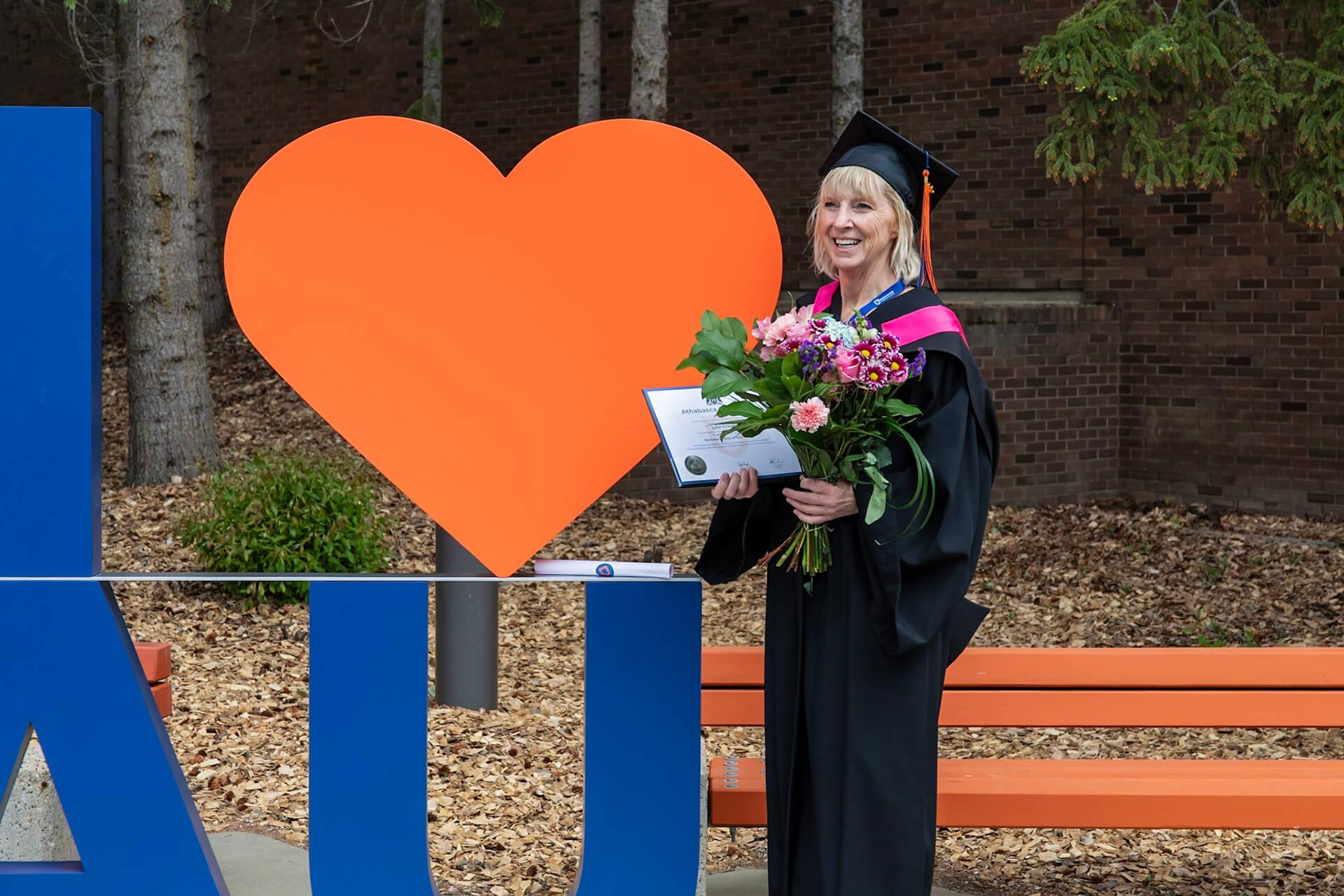 a grad holds their degree in front of an I love AU sign