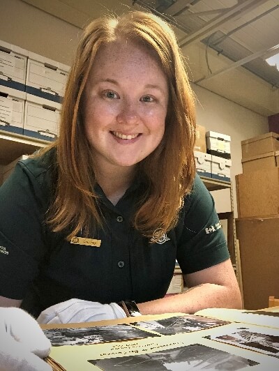 Courtney King wearing white gloves turning the pages of archival photos wearing a Parks Canada uniform.