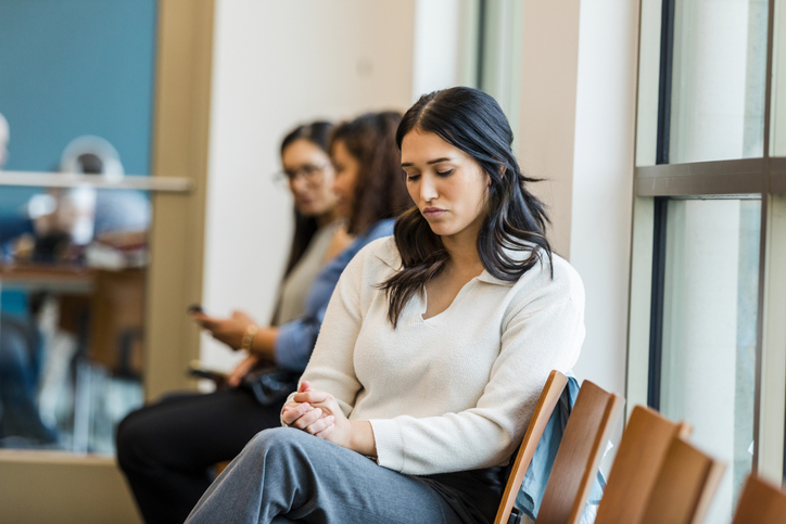 Young woman sits alone, lost in thought, in a waiting area.