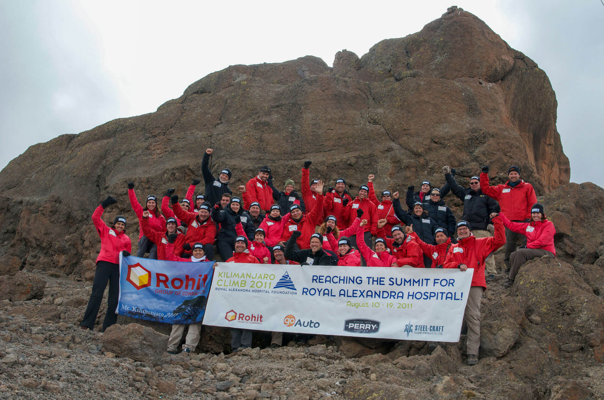 group of climbers hold a sign atop Mount Kilimanjaro