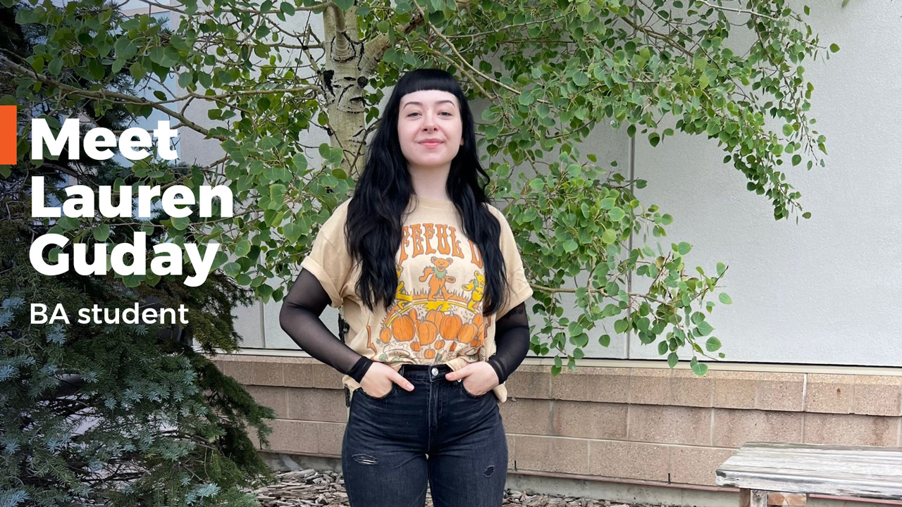 Lauren Guday standing outside in front of a building and trees with her hands in her pockets