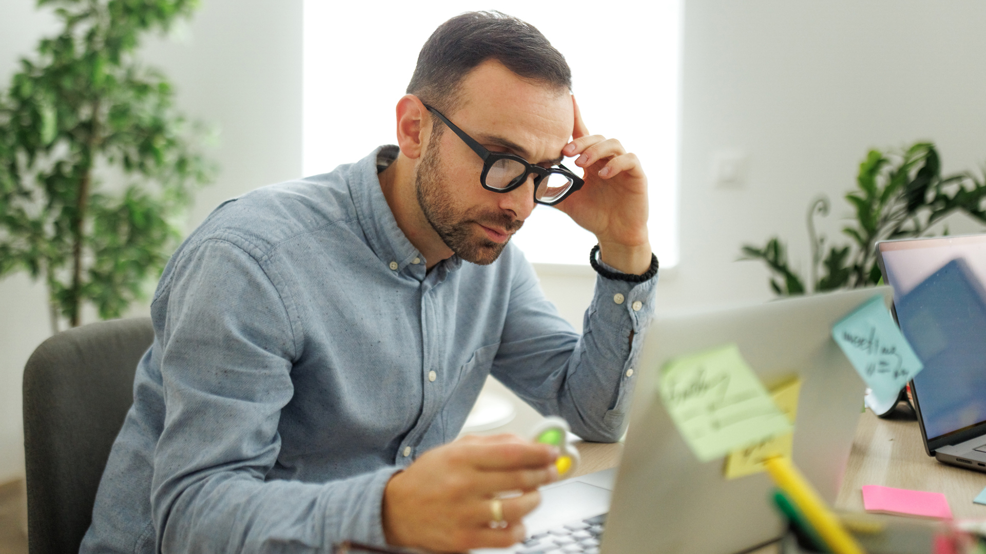Adult learner sitting at a desk reading his computer holding a fidget spinner