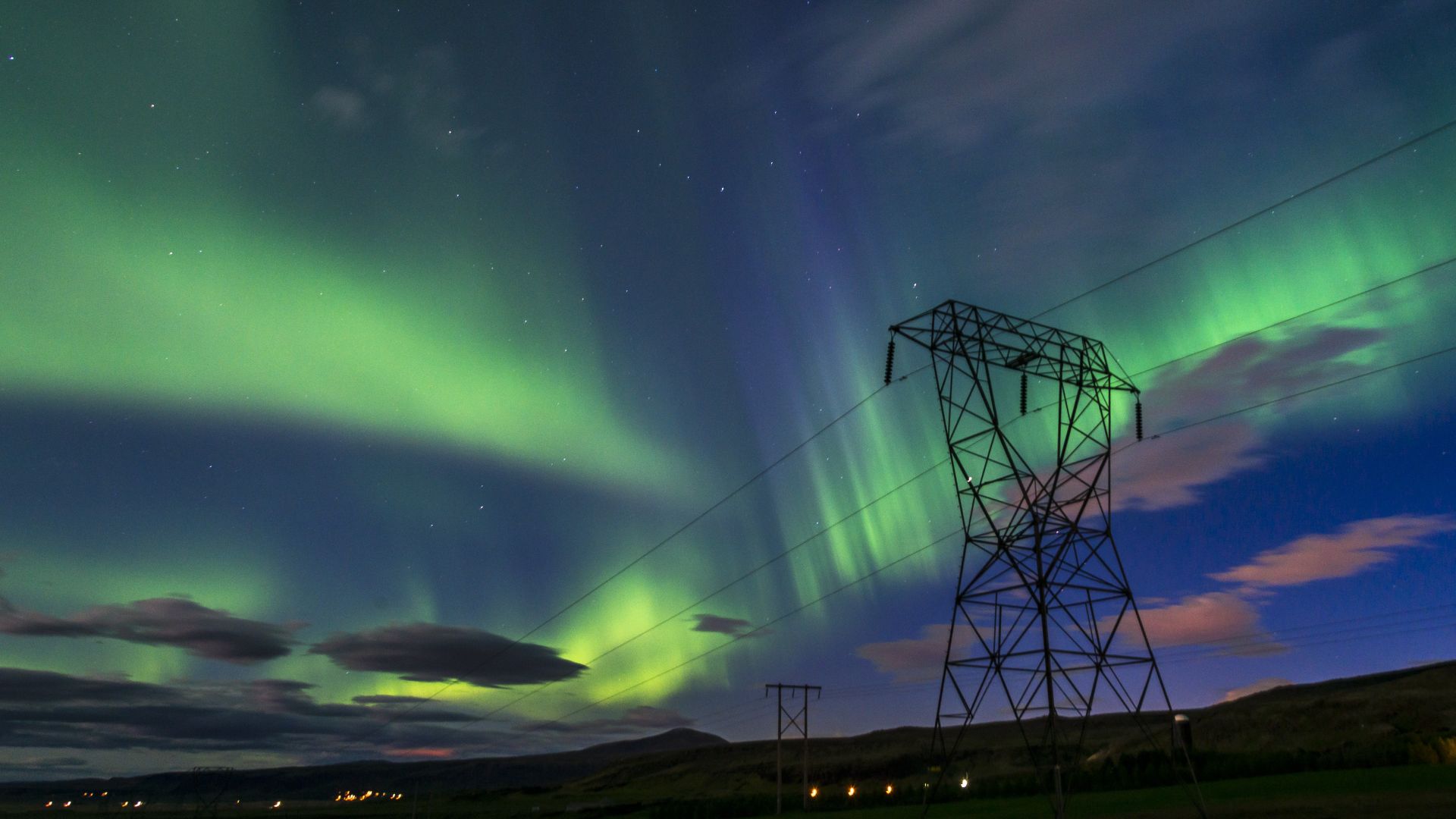 Aurora borealis is seen in the night sky with power lines in the foreground