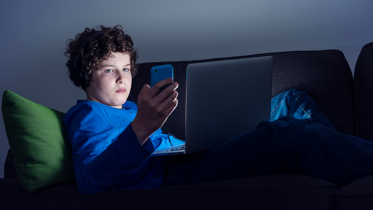 Teen on multiple screens sitting in a dark room