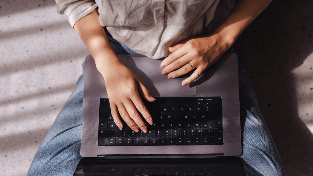 A from above view of person typing on their laptop while sitting on the floor.