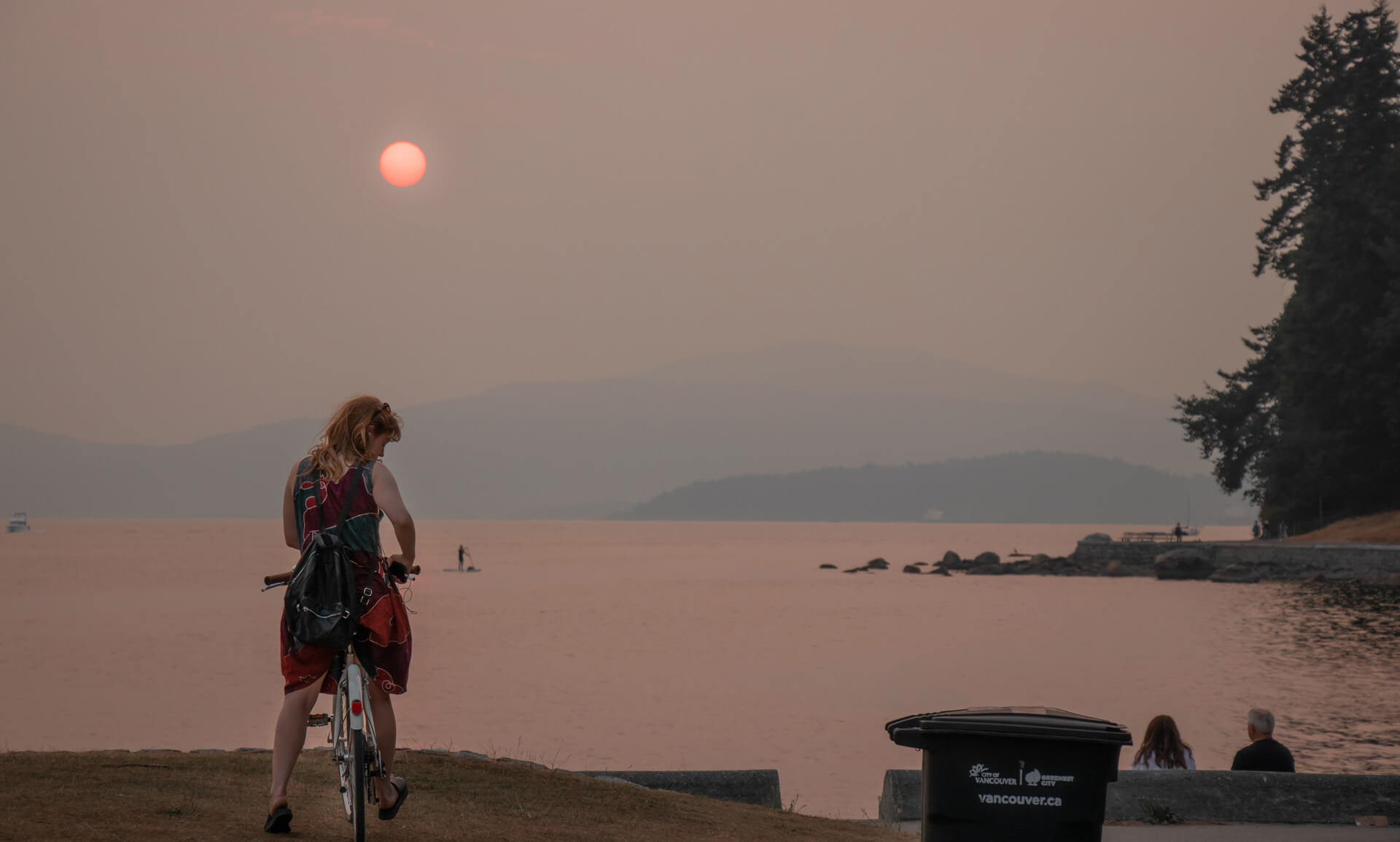 cyclist in Vancouver looks across the harbour with wildfire smoke on the horizon