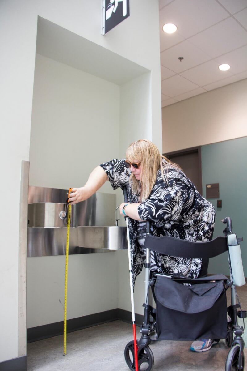 A woman is shown taking a measurement to determine accessibility in a building.