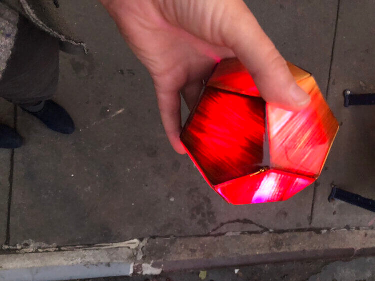 Reddish-orange light orb in a person's hand over a sidewalk