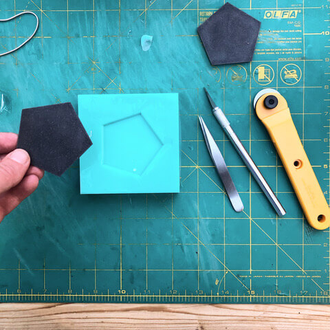 Black geometric shape with tools on a cutting mat.