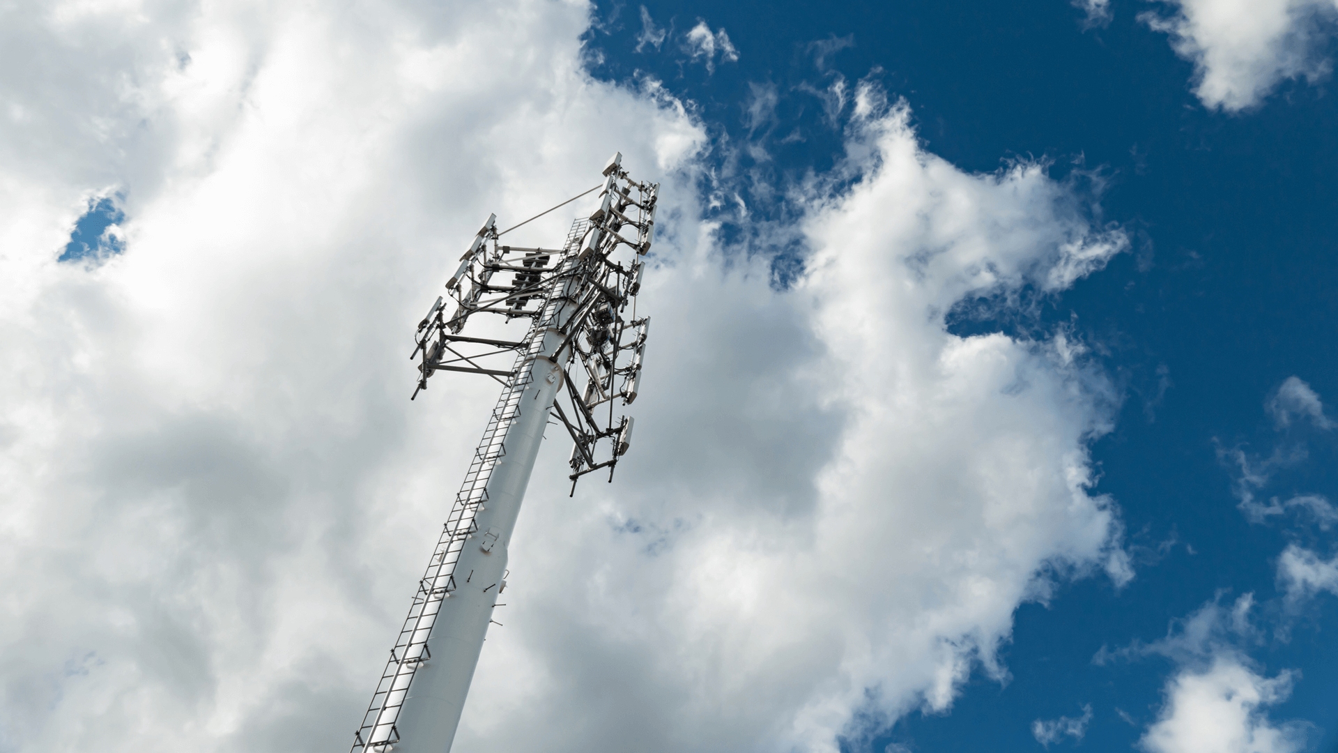 worm's eye view of a cellphone tower and a blue sky with clouds