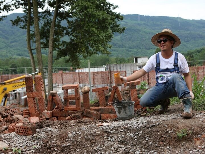 Dr. Henry Tsang next to a pile of bricks arranged to spell out 
