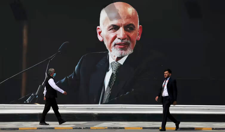 People walk near a mural of President Ashraf Ghani at Hamid Karzai International Airport, in Kabul, Afghanistan. Ghani fled the country in August 2021. (AP Photo/Rahmat Gul)