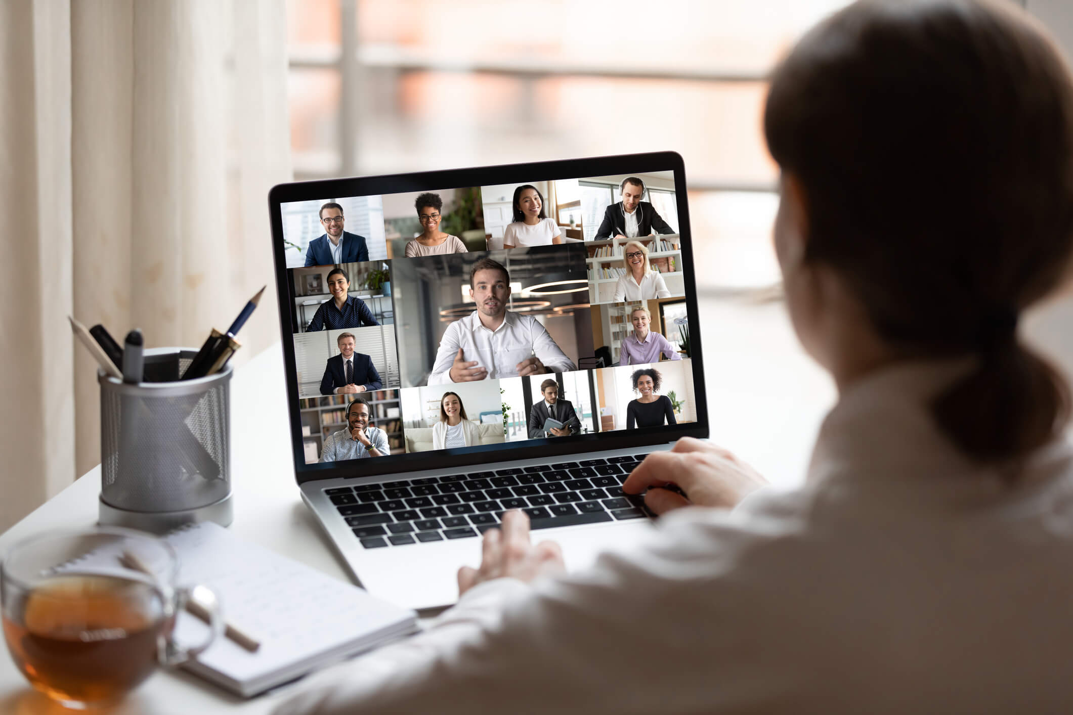A person looking at a laptop screen, on which we can see a diverse group of people on a videoconference