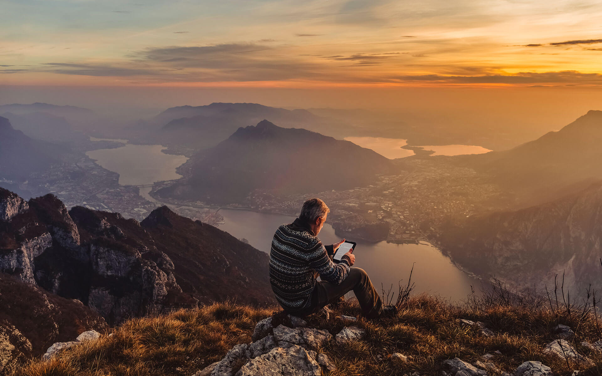 a man reading atop a mountain at sunset