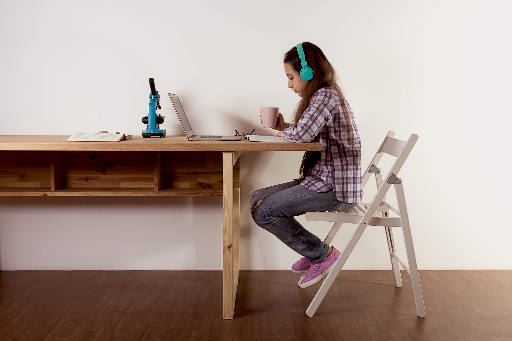 Distance learning. Home schooling, young teen girl studying at a laptop, listening to music with headphones, watching a webinar online, doing science and biology. Elearning concept