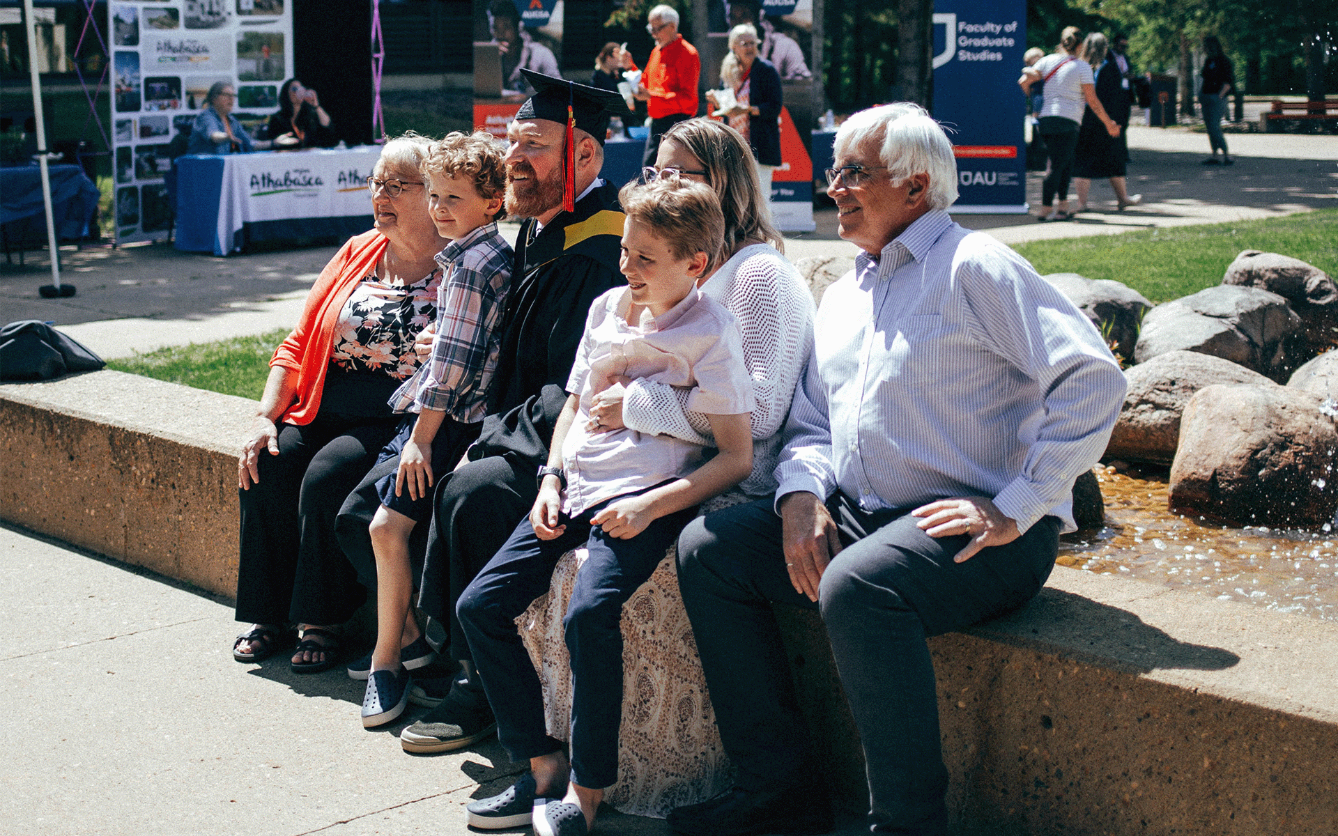 Family at Fountain A family surrounds a graduate while sitting near the fountains on Athabasca University campus