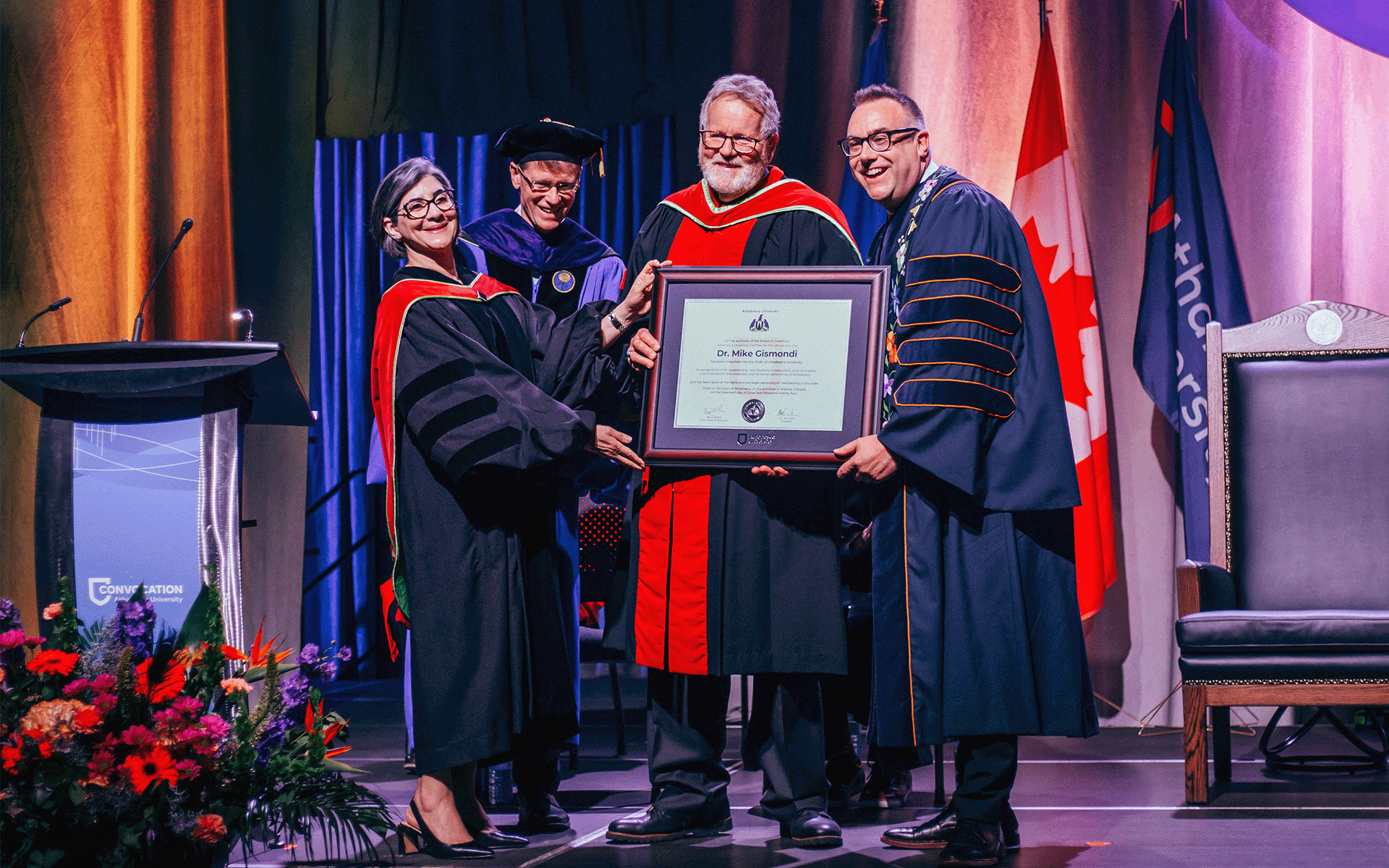 Mike Gismondi A woman and three men standing together with one of them holding a large framed document for the Order of Athabasca University awarded to Dr. Mike Gismondi during the convocation ceremony
