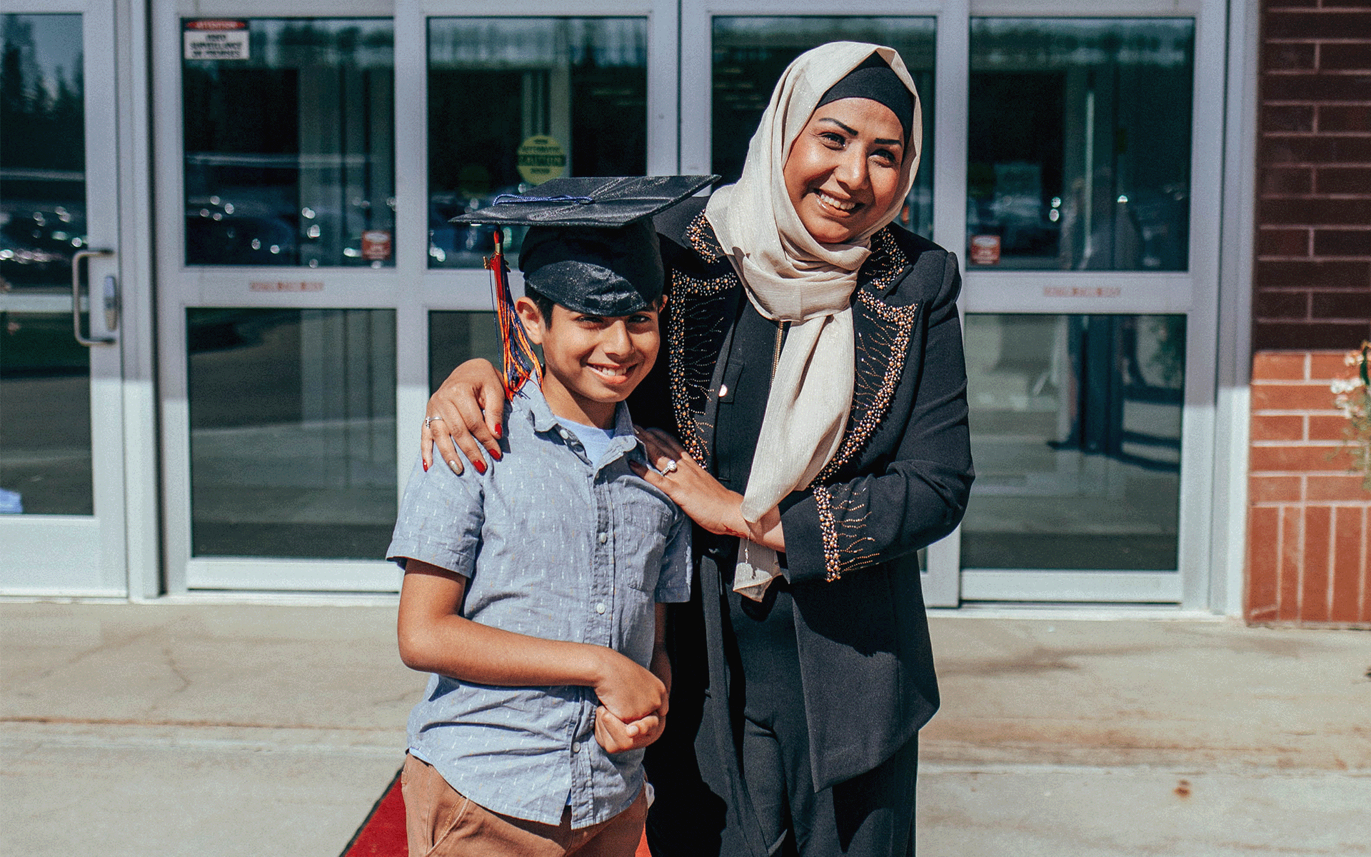 Proud family Young boy wearing grad cap and woman standing next to him. Both of them are smiling at the camera