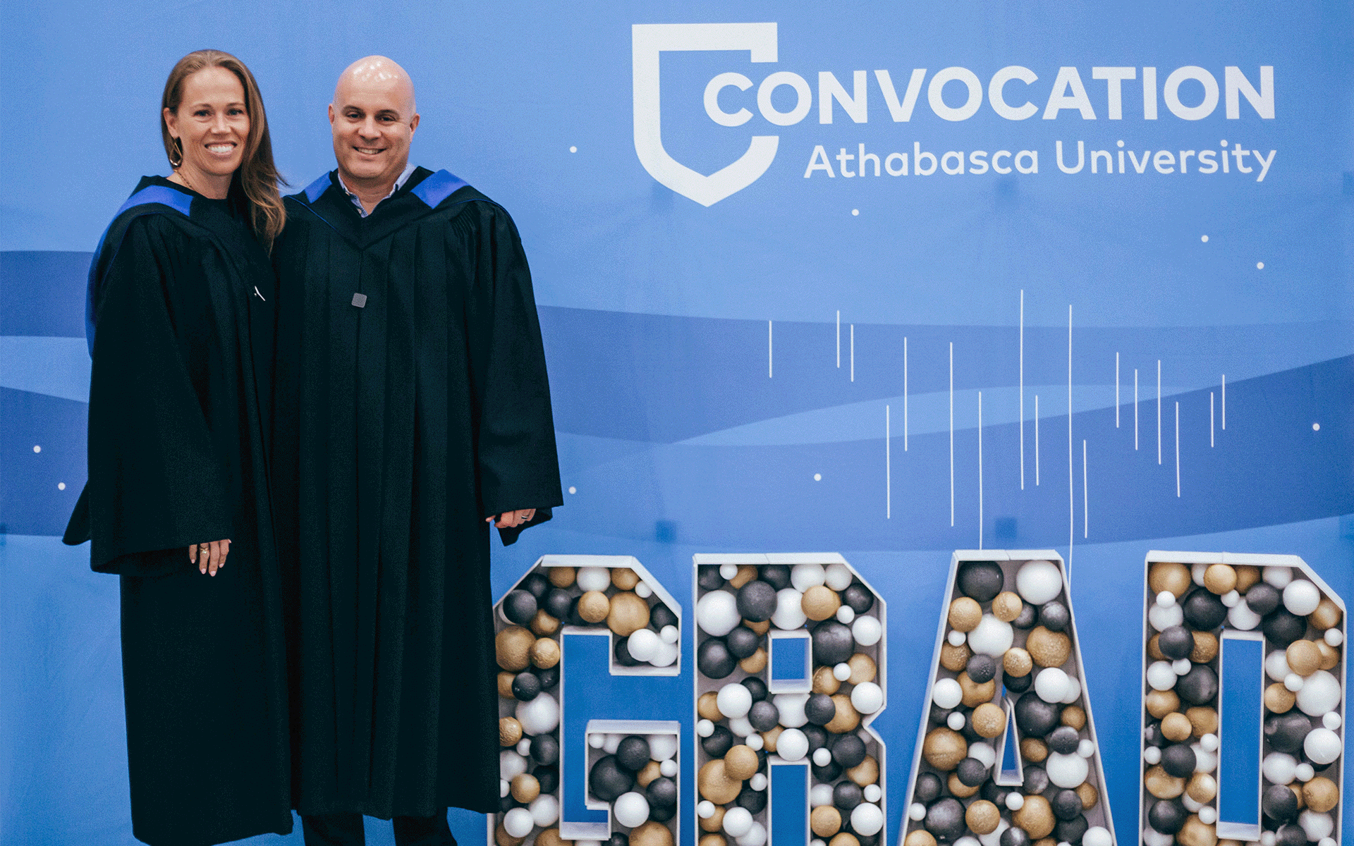 ainsley and daniel clement a man and woman who are both graduates standing in front of a convocation sign