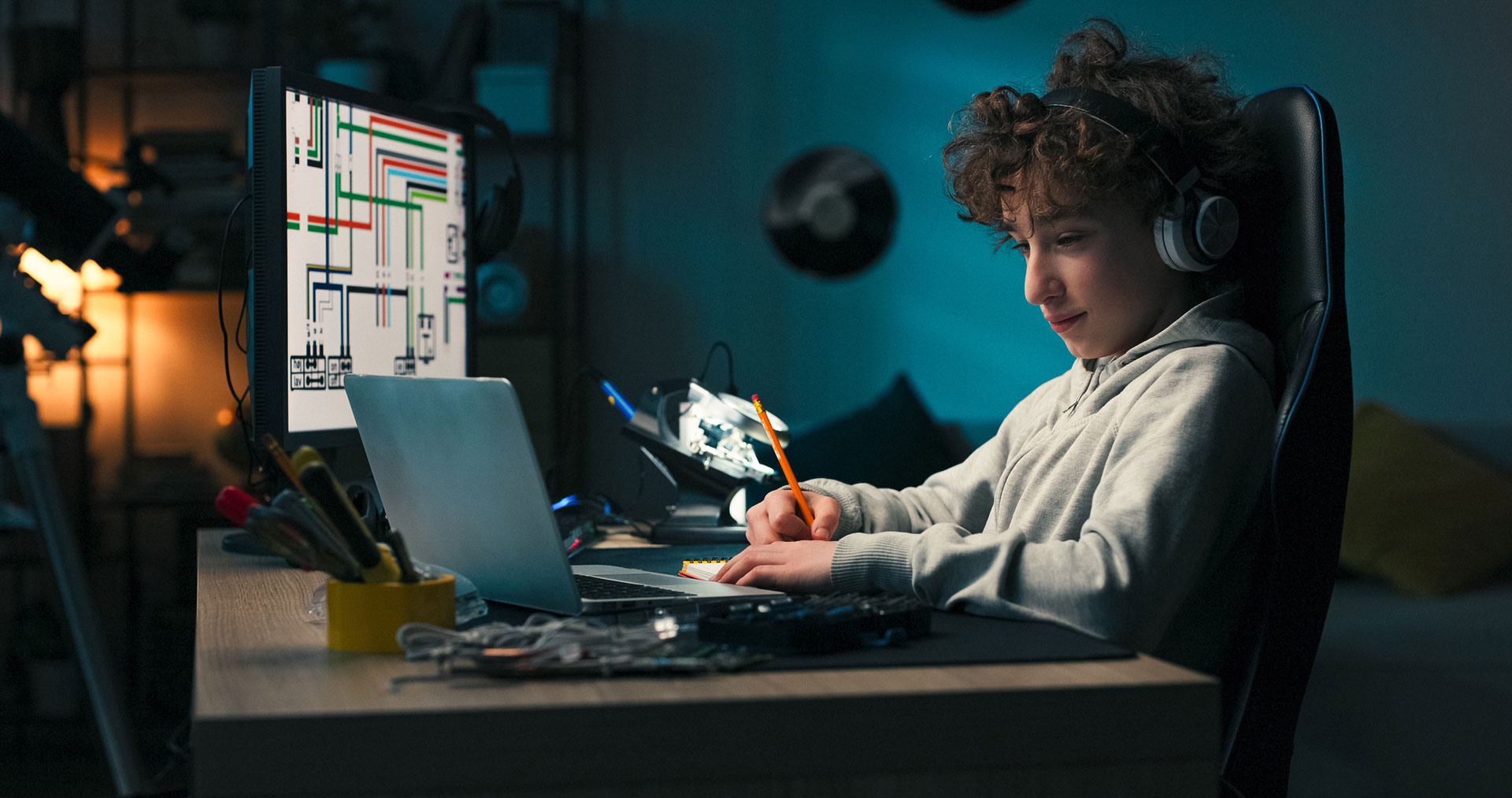 A high school student working on a laptop while wearing headphones